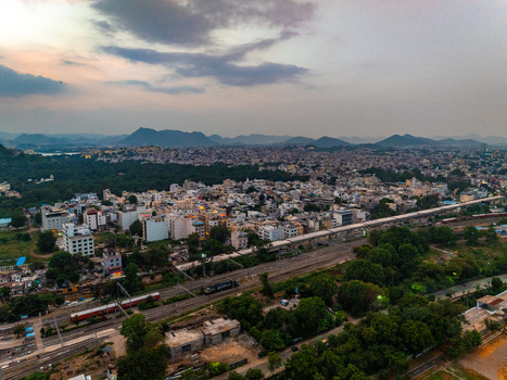 Aerial view of the cityscape of Udaipur with railway tracks dense urban buildings and distant hills under a cloudy sky in Udaipur Rajasthan India. Aerial view of the cityscape of Udaipur with railway tracks dense urban buildings and distant hills under a cloudy sky in Udaipur Rajasthan India.