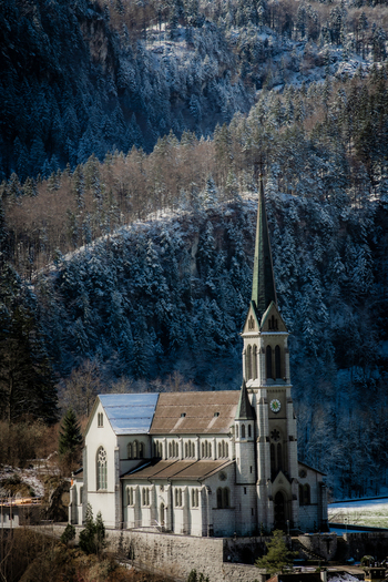 View of a Gothic church stands tall against a backdrop of snow dusted mountains creating a serene winter landscape from a train Train from Lucerne to Interlaken Switzerland. View of a Gothic church stands tall against a backdrop of snow dusted mountains creating a serene winter landscape from a train Train from Lucerne to Interlaken Switzerland.