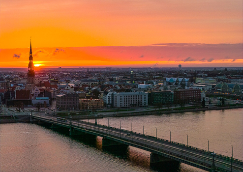 Aerial view of the historic skyline featuring the spire of St. Peter s Church and the Stone Bridge crossing the Daugava River during a vibrant sunset in Riga Latvia. Aerial view of the historic skyline featuring the spire of St. Peter s Church and the Stone Bridge crossing the Daugava River during a vibrant sunset in Riga Latvia.