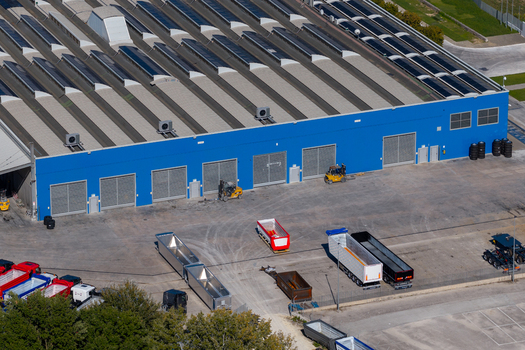 Aerial view of an industrial facility with a blue facade and sawtooth roof featuring forklifts and parked semi truck trailers in the yard in Spoleto Umbria Italy. Aerial view of an industrial facility with a blue facade and sawtooth roof featuring forklifts and parked semi truck trailers in the yard in Spoleto Umbria Italy.
