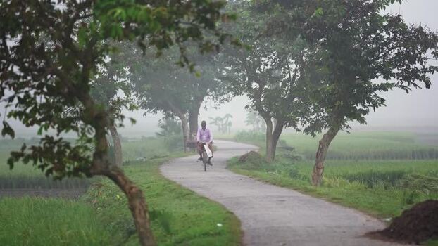 View of a man riding a bicycle on a rural road Bangladesh.