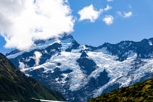 View of snow capped peaks pierce the sky glaciers cascade down rugged slopes under a bright sky framed by vibrant green foliage Mount Cook Canterbury Region New Zealand. View of snow capped peaks pierce the sky glaciers cascade down rugged slopes under a bright sky framed by vibrant green foliage Mount Cook Canterbury Region New Zealand.