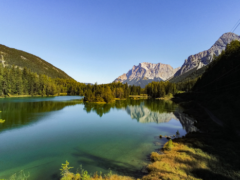 Aerial view of Mittersee lake surrounded by dense pine forests and dramatic mountain peaks under a clear blue sky in Biberwier Tirol Austria.