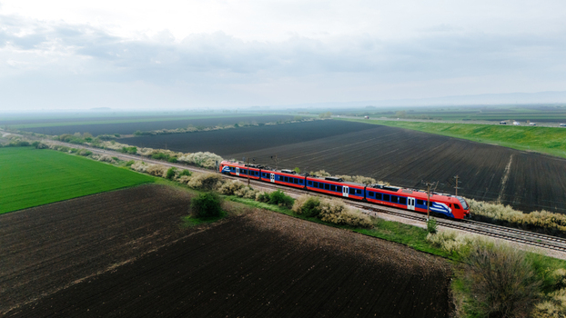 Aerial view of a vibrant red and blue train cuts through the landscape contrasting against the dark ploughed fields and verdant green patches Sremska Mitrovica Vojvodina Serbia. Aerial view of a vibrant red and blue train cuts through the landscape contrasting against the dark ploughed fields and verdant green patches Sremska Mitrovica Vojvodina Serbia.