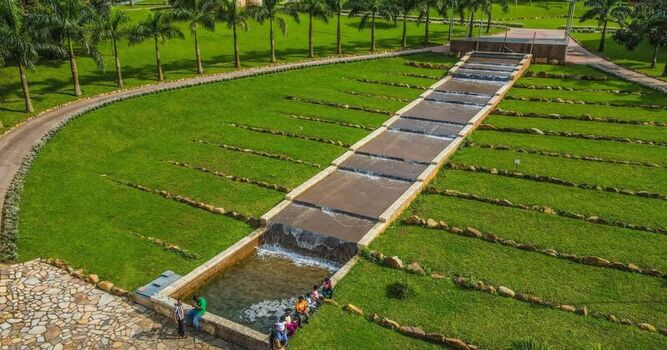 Aerial view of a tiered water cascade in a lush green park with palm trees and people sitting along the stone edge in Ghana. Aerial view of a tiered water cascade in a lush green park with palm trees and people sitting along the stone edge in Ghana.