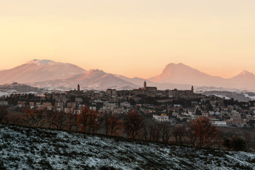View of the historic town of Corridonia nestled in a snowy landscape with mountains in the background under a warm sunset glow in Corridonia Marche Italy.