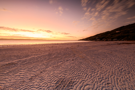 View of Quaranup Beach at sunset with rippled sand patterns on the shore and a calm sea under a soft orange sky in Vancouver Peninsula Western Australia Australia. View of Quaranup Beach at sunset with rippled sand patterns on the shore and a calm sea under a soft orange sky in Vancouver Peninsula Western Australia Australia.