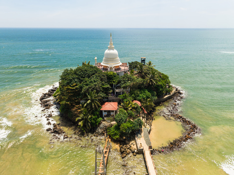 Aerial view of the Parewi Duwa Temple with its iconic white stupa on a lush green island surrounded by the turquoise waters of the Indian Ocean in Matara Sri Lanka. Aerial view of the Parewi Duwa Temple with its iconic white stupa on a lush green island surrounded by the turquoise waters of the Indian Ocean in Matara Sri Lanka.