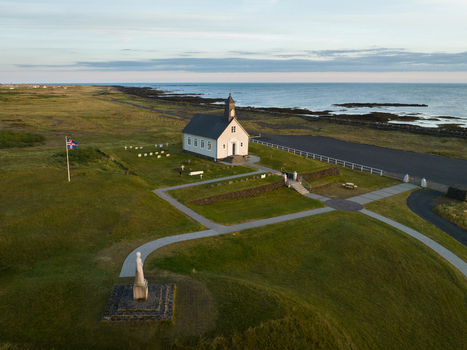 Aerial view of a white church standing gracefully by the ocean its steeple reaching towards the clear sky contrasted against the rugged coastline Iceland Sveitarf&eacute;lagi&eth; &Ouml;lfus Iceland.