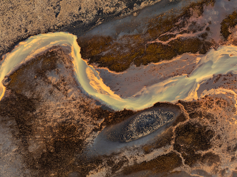 Aerial view of a glacial river with braided channels and sediment flowing through dark volcanic terrain in Iceland. Aerial view of a glacial river with braided channels and sediment flowing through dark volcanic terrain in Iceland.