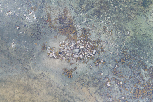 Aerial view of a rocky outcrop surrounded by shallow coastal waters with seaweed and pebbles in Unalaska Alaska United States.