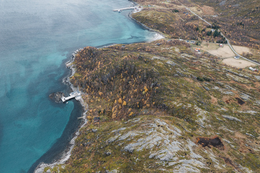 Aerial view of the rugged coastline of Senja with rocky terrain autumn foliage and a small pier extending into the turquoise water in Senja Troms Norway.