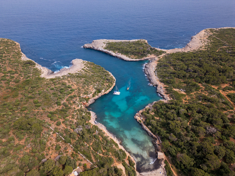 Aerial view of Cala Sa Nau cove with turquoise waters rocky cliffs and a white boat anchored near the shore in Felanitx Balearic Islands Spain. Aerial view of Cala Sa Nau cove with turquoise waters rocky cliffs and a white boat anchored near the shore in Felanitx Balearic Islands Spain.