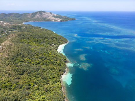 Aerial view of the lush green hills of the island meeting the turquoise Caribbean Sea with coral reefs visible under the water in Guanaja Bay Islands Department Honduras. Aerial view of the lush green hills of the island meeting the turquoise Caribbean Sea with coral reefs visible under the water in Guanaja Bay Islands Department Honduras.
