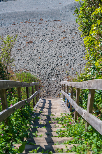 View of the wooden staircase leading down to the pebble beach at Portnadler Bay along the South West Coastal Path in Looe Cornwall United Kingdom. View of the wooden staircase leading down to the pebble beach at Portnadler Bay along the South West Coastal Path in Looe Cornwall United Kingdom.