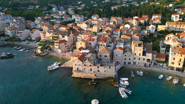 Aerial view of the historic coastal town of Komiza with traditional stone houses red tiled roofs and boats in the turquoise harbor Komiza Split Dalmatia County Croatia.