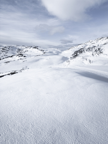 Aerial view of snow covered mountain slopes and rolling hills under a cloudy winter sky in the arctic wilderness Kvaloya Troms Norway. Aerial view of snow covered mountain slopes and rolling hills under a cloudy winter sky in the arctic wilderness Kvaloya Troms Norway.
