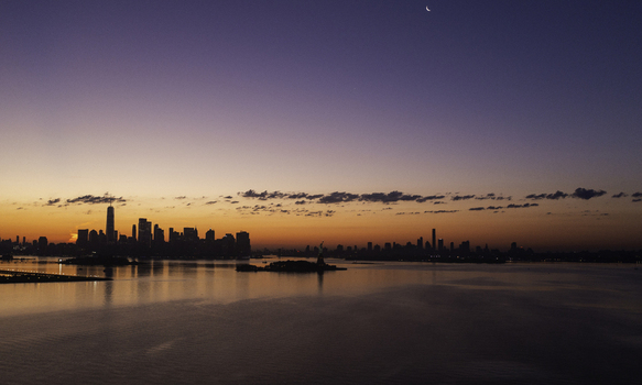 Aerial view of the New York City skyline at sunset with the Statue of Liberty visible in the harbor reflecting on the calm water under a twilight sky in New York New York United States.