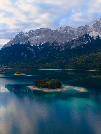 Aerial view of the turquoise Eibsee lake with small islands at the foot of the Zugspitze mountains and dense forests in Grainau Bavaria Germany. Aerial view of the turquoise Eibsee lake with small islands at the foot of the Zugspitze mountains and dense forests in Grainau Bavaria Germany.
