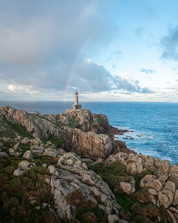 Aerial view of Faro de Punta Nariga lighthouse standing on rugged granite cliffs with a rainbow arching over the Atlantic Ocean under a cloudy sky Malpica A Coruna Spain. Aerial view of Faro de Punta Nariga lighthouse standing on rugged granite cliffs with a rainbow arching over the Atlantic Ocean under a cloudy sky Malpica A Coruna Spain.