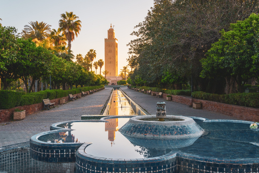View of the Koutoubia Mosque minaret rising above a tranquil park with a decorative fountain lush palm trees and orange trees in the golden hour light in Marrakesh Marrakesh Safi Morocco. View of the Koutoubia Mosque minaret rising above a tranquil park with a decorative fountain lush palm trees and orange trees in the golden hour light in Marrakesh Marrakesh Safi Morocco.