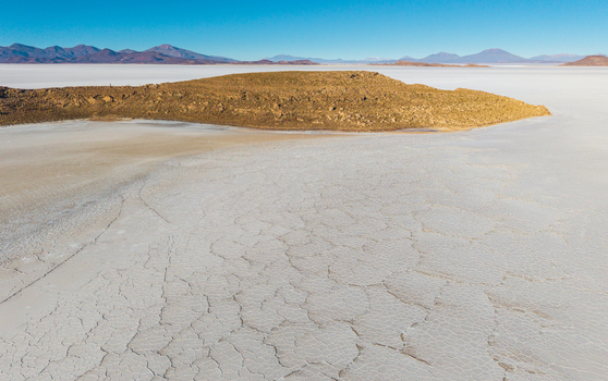 Aerial view of the vast Uyuni Salt Flat with its iconic hexagonal salt crust patterns and a rocky island under a clear blue sky in Uyuni Potosi Department Bolivia. Aerial view of the vast Uyuni Salt Flat with its iconic hexagonal salt crust patterns and a rocky island under a clear blue sky in Uyuni Potosi Department Bolivia.