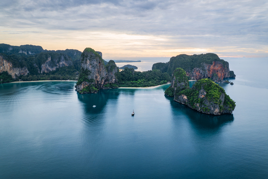 Aerial view of Railay Beach with its iconic limestone cliffs rising from the turquoise Andaman Sea featuring a small boat in the calm water in Ao Nang Krabi Thailand. Aerial view of Railay Beach with its iconic limestone cliffs rising from the turquoise Andaman Sea featuring a small boat in the calm water in Ao Nang Krabi Thailand.