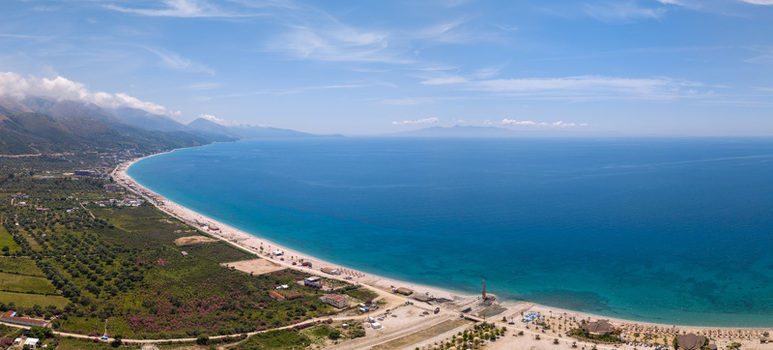 Aerial view of the long sandy Borsh Beach and turquoise Ionian Sea coastline with olive groves and green hills under a blue sky in Borsh Vlore County Albania. Aerial view of the long sandy Borsh Beach and turquoise Ionian Sea coastline with olive groves and green hills under a blue sky in Borsh Vlore County Albania.