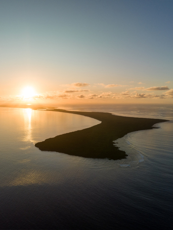 Aerial view of a dark island stretching out into a tranquil blue sea under a radiant sunrise Ouvéa Loyalty Islands Province New Caledonia. Aerial view of a dark island stretching out into a tranquil blue sea under a radiant sunrise Ouvéa Loyalty Islands Province New Caledonia.