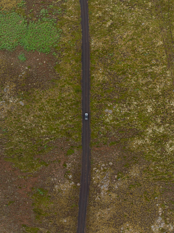Aerial view of a lone car driving along a narrow dirt road through the vast mossy landscape of the Icelandic highlands in Raufarhofn Nordurthing Iceland.