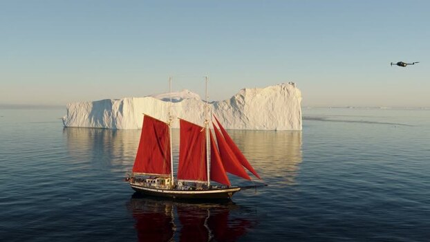 Aerial view of sailboat with red sails near iceberg Greenland. Aerial view of sailboat with red sails near iceberg Greenland.