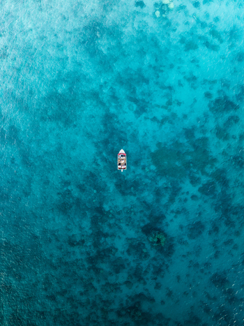 Aerial view of a solitary boat cutting through the mesmerizing turquoise waters creating a stunning contrast against the clear sea bottom Noumea New Caledonia. Aerial view of a solitary boat cutting through the mesmerizing turquoise waters creating a stunning contrast against the clear sea bottom Noumea New Caledonia.