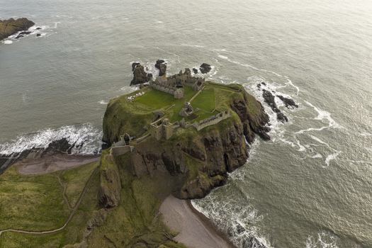 Aerial view of the medieval ruins of Dunnottar Castle perched on a dramatic rocky headland surrounded by the North Sea and steep cliffs in Stonehaven Scotland United Kingdom. Aerial view of the medieval ruins of Dunnottar Castle perched on a dramatic rocky headland surrounded by the North Sea and steep cliffs in Stonehaven Scotland United Kingdom.
