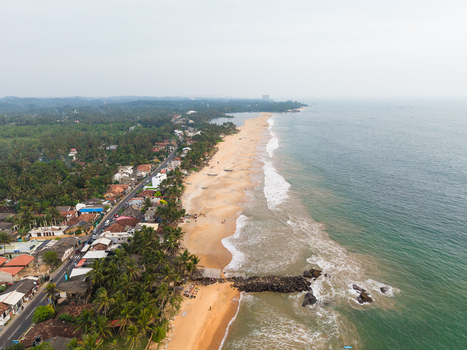 Aerial view of the sandy coastline with palm trees coastal road and houses along the turquoise ocean waves in Galle Southern Province Sri Lanka.