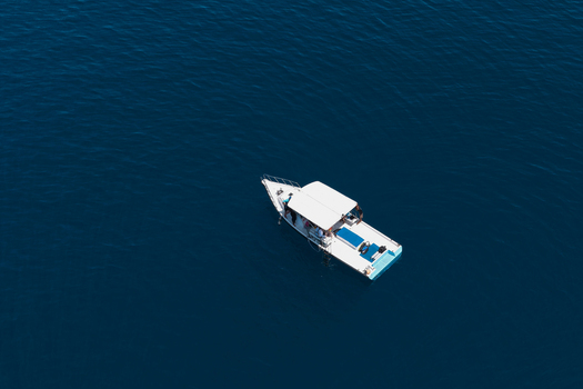 Aerial view of a white motorboat with a canopy carrying passengers on the deep blue ocean waters near Muraidhoo Haa Alif Atoll Maldives. Aerial view of a white motorboat with a canopy carrying passengers on the deep blue ocean waters near Muraidhoo Haa Alif Atoll Maldives.