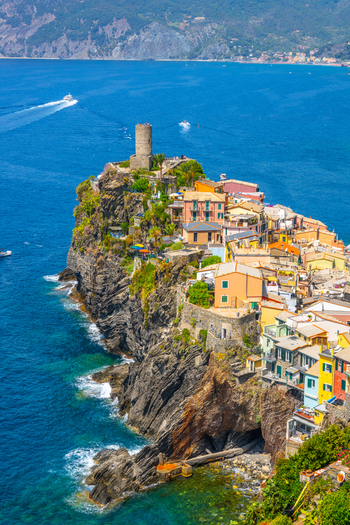 View of the colorful houses and historic stone tower of Vernazza in Cinque Terre perched on a rocky cliff above the Mediterranean sea in Vernazza Liguria Italy.