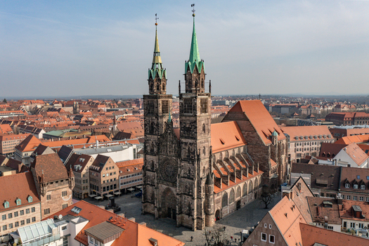 Aerial view of St. Lorenz church with its twin Gothic spires and red tiled roof surrounded by the historic old town rooftops under a clear blue sky Nurnberg Bayern Germany.