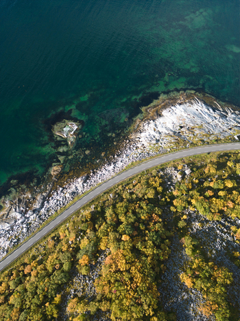 Aerial view of a coastal road winding along the rocky shoreline of Vik Strand with turquoise water and autumn foliage in Leknes Nordland Norway. Aerial view of a coastal road winding along the rocky shoreline of Vik Strand with turquoise water and autumn foliage in Leknes Nordland Norway.