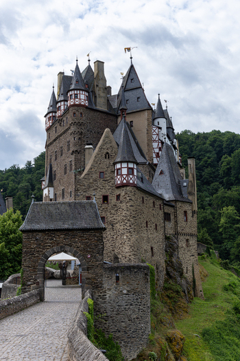 View of Eltz Castle featuring medieval stone architecture with pointed turrets and half timbered details nestled in a lush forest Wierschem Rhineland Palatinate Germany.