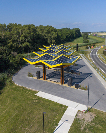 Aerial view of the Fastned Charging Station featuring distinctive yellow solar panel roofs located near a road with surrounding greenery in Lelystad Flevoland Netherlands. Aerial view of the Fastned Charging Station featuring distinctive yellow solar panel roofs located near a road with surrounding greenery in Lelystad Flevoland Netherlands.