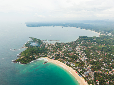 Aerial view of the sandy coastline and turquoise waters of the Indian Ocean beach surrounded by lush tropical greenery Mirissa Southern Province Sri Lanka. Aerial view of the sandy coastline and turquoise waters of the Indian Ocean beach surrounded by lush tropical greenery Mirissa Southern Province Sri Lanka.