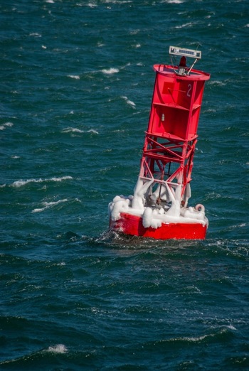 View of a red navigational buoy covered in ice floating in the choppy blue waters of Martha s Vineyard in Edgartown Massachusetts United States.