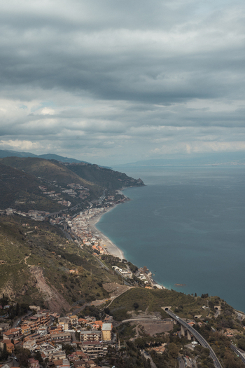 View of the stunning coastline where the town meets the sea under a cloudy sky a serene blend of architecture and nature Taormina Sicily Italy.