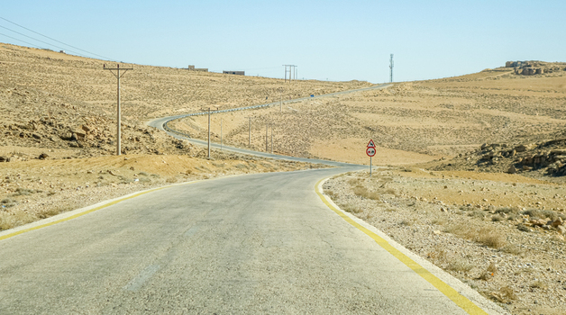View of the winding asphalt road through the arid landscape of the Wadi Rum Desert in Wadi Rum Village Aqaba Governorate Jordan. View of the winding asphalt road through the arid landscape of the Wadi Rum Desert in Wadi Rum Village Aqaba Governorate Jordan.