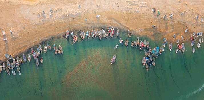 Aerial view of numerous colorful wooden fishing boats moored along the sandy shoreline in turquoise coastal waters in Gwadar Balochistan Pakistan.