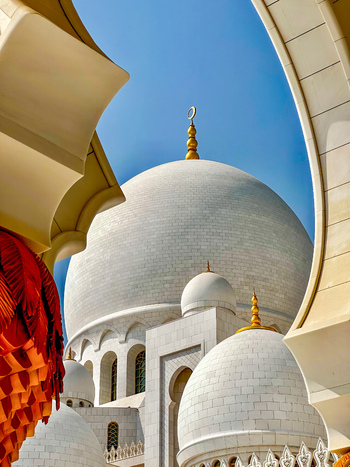 Abu Dhabi United Arab Emirates 15 October 2023 View of the white marble domes and golden finials of the Sheikh Zayed Grand Mosque framed by ornate arches against a clear blue sky.