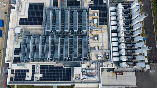 Aerial view of a hyperscale data center featuring rows of cooling units industrial ventilation systems and solar panel arrays on the rooftop in Melegnano Lombardy Italy.