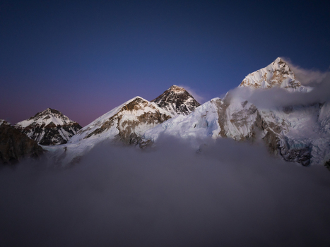 Aerial view of Mount Everest with snow capped peaks rising above a sea of clouds under a twilight sky in Nepal.