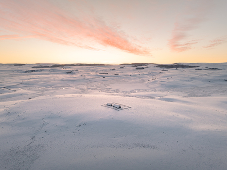 Aerial view of a snow covered landscape with a solitary typical buron house beneath a pastel sunrise Nasbinals Occitanie France.