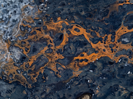 Aerial view of a volcanic landscape featuring intricate patterns of dark basaltic rock and vibrant orange mineral deposits in Iceland. Aerial view of a volcanic landscape featuring intricate patterns of dark basaltic rock and vibrant orange mineral deposits in Iceland.